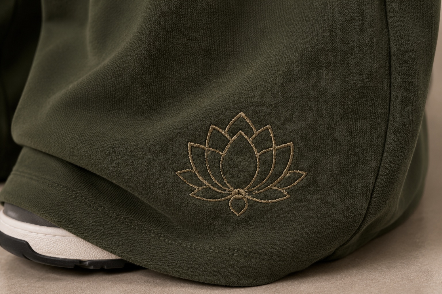 Close-up of the lotus embroidery on the hem of the Lotus Original Green tracksuit bottoms.