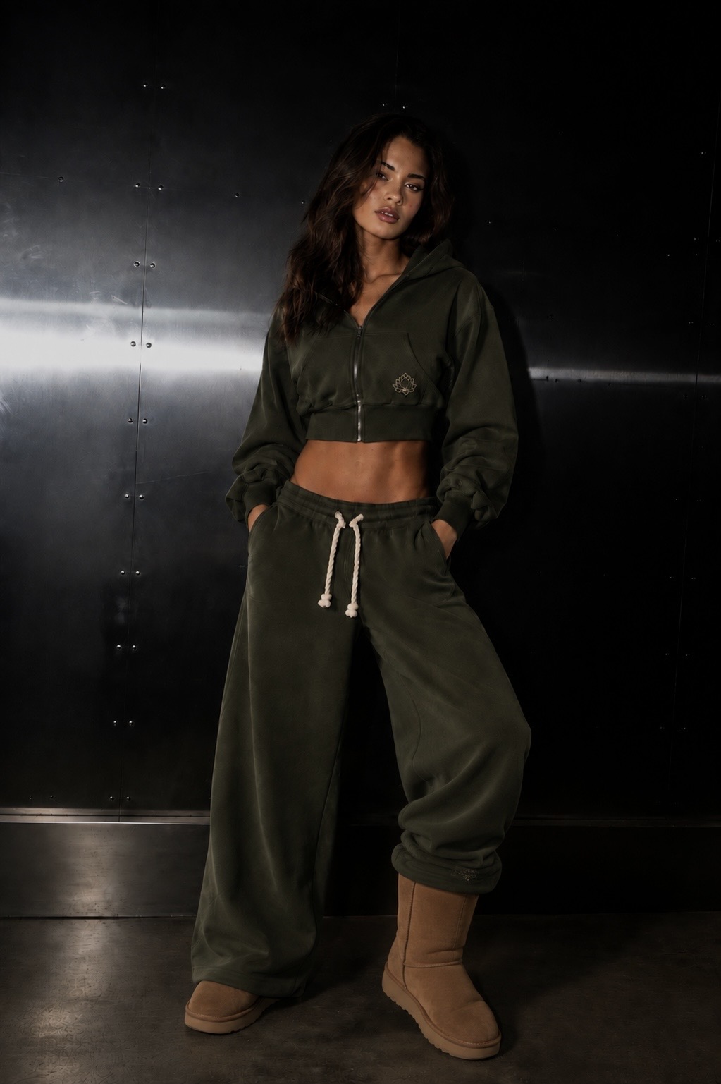 Model against a steel wall wearing the olive Lotus Original cropped zip up and wide-leg bottoms.