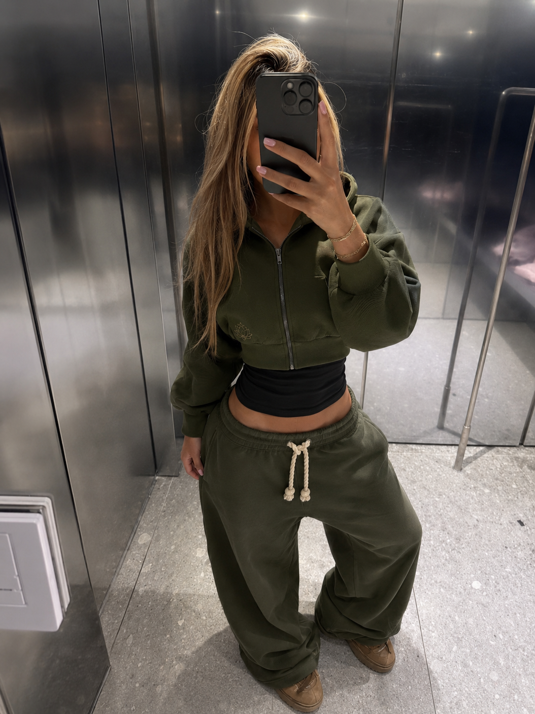 Customer taking a mirror selfie in a lift wearing the olive Lotus Original tracksuit.